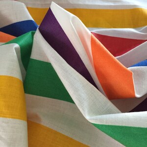 May include: A colorful striped fabric with alternating white, green, yellow, orange, red, purple, and blue stripes. The fabric is folded and draped, showing the different colors and patterns.