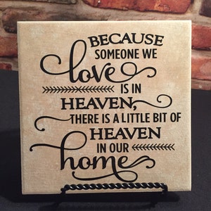 May include: A beige ceramic tile with black lettering that reads "Because someone we love is in heaven, there is a little bit of heaven in our home".