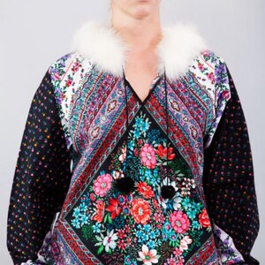 Könnte beinhalten: Gemustertes Oberteil mit weißem Pelzkragen. Das Oberteil hat ein florales Design in der Mitte, schwarze Ärmel mit kleinen Blumenmustern und weiße Manschetten. Der Stil ist Vintage, mit einem lebendigen und farbenfrohen Design.