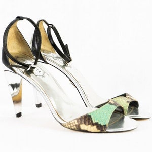 Könnte beinhalten: Ein Paar schwarze und grüne Sandalen mit Absatz, silberner Plattform und Knöchelriemen. Die Sandalen haben ein Schlangenhautmuster.