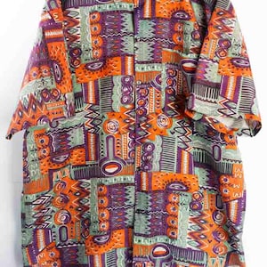 Könnte beinhalten: Kurzärmeliges Hemd mit auffälligem geometrischem Muster. Das Hemd zeigt eine Collage aus orangefarbenen, lila und grünen Formen. Kragen und Knopfleiste sind sichtbar und unterstreichen das Design.
