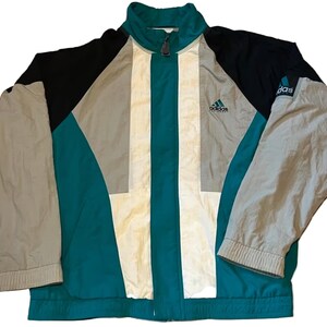 Könnte beinhalten: Vintage Adidas Equipment Jacke im Colorblock-Design. Die Jacke hat ein Farbschema aus Teal, Schwarz, Grau und Creme. Das Adidas-Logo ist auf der Brust sichtbar. Die Jacke hat einen durchgehenden Reißverschluss und einen hohen Kragen.