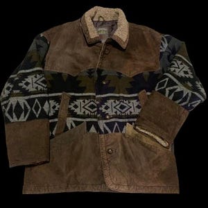 May include: A brown suede jacket with a patterned fabric design on the sleeves and upper chest. The jacket has a shearling collar and two front pockets. The fabric design includes geometric shapes in shades of gray, black, and olive green.