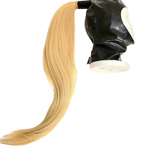 May include: A black latex ponytail holder with a blonde ponytail attached. The ponytail holder is on a white foam mannequin head.