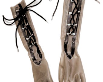 Puede incluir: Un par de guantes largos de goma transparente con cordones negros y ojales plateados. Los guantes están atados en la muñeca.