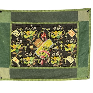May include: A rectangular, embroidered textile with a dark background and a green border. The central design features playing cards, flowers, and a pipe. The color palette includes green, yellow, red, and white, creating a detailed and decorative piece.