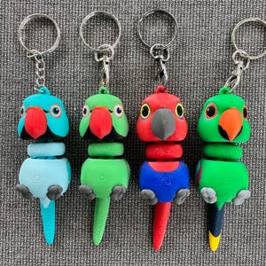 Puede incluir: Cuatro llaveros de loros coloridos. Cada loro tiene una combinación de colores única: turquesa, verde, rojo y verde. Tienen picos rojos, patas negras y están unidos a llaveros plateados. Los loros son de plástico.
