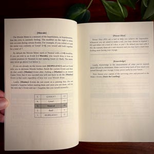 May include: An open instruction manual with black text on white pages. The left page details a Morale Meter with a table ranging from 1 to 5, labeled Godly to Hopeless. The right page explains Power Dice and Knowledge mechanics for a tabletop game.