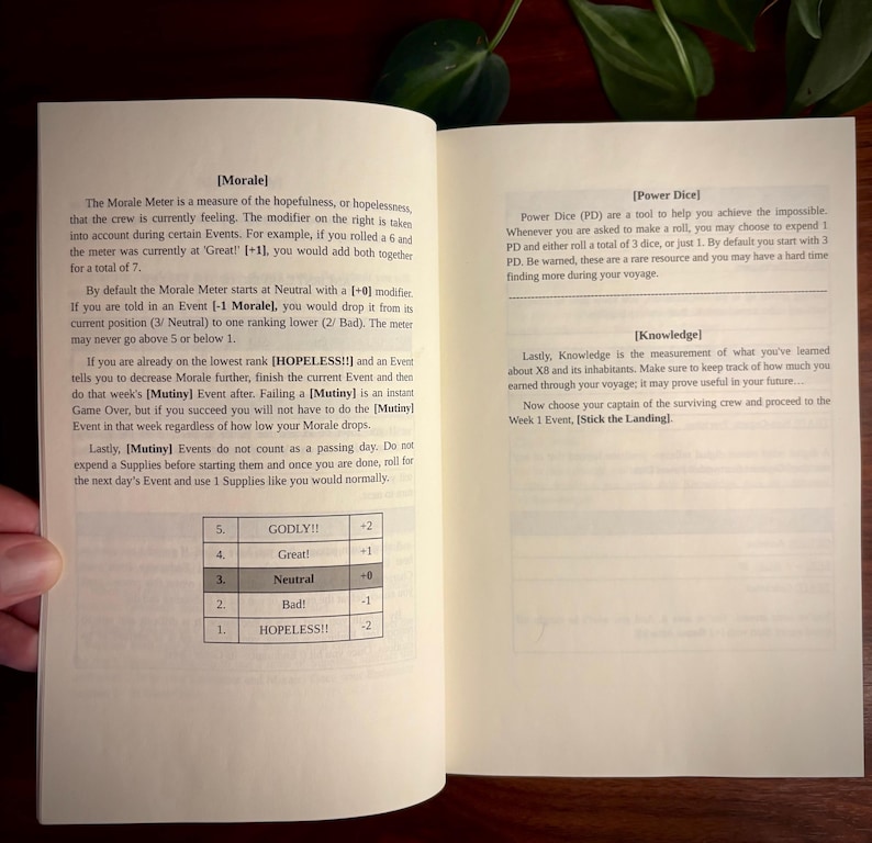 May include: An open instruction manual with black text on white pages. The left page details a Morale Meter with a table ranging from 1 to 5, labeled Godly to Hopeless. The right page explains Power Dice and Knowledge mechanics for a tabletop game.