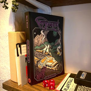 May include: A black book titled Voyager: Escape from X8 by Nat E. Wood with a graphic illustration of a crashed spacecraft on a dark landscape. The book is positioned next to a stack of floppy disks and two translucent red six-sided dice.