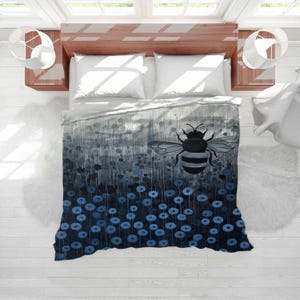 May include: A duvet cover featuring a large bee illustration with gray and black stripes, set against a backdrop of blue and gray floral patterns. The bedding has a watercolor effect, with a white top sheet and pillows.