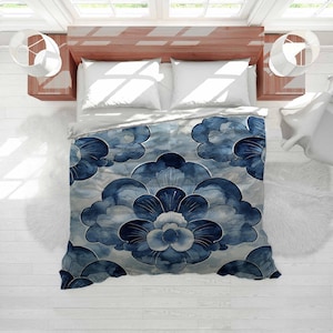 May include: A duvet cover with a blue and white floral pattern. The design features large, stylized flowers in shades of blue against a light blue and white background. The bed is in a bright room with white walls and a wooden bed frame.