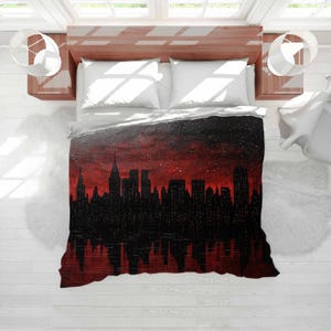 May include: A black and red city skyline design on a bedspread. The design features a silhouette of buildings against a red and black sky, with a reflection of the skyline below. The bedspread is on a bed with white pillows and a wooden frame.