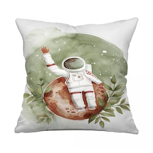 May include: White square throw pillow featuring an astronaut waving from a reddish-brown planet. The astronaut is wearing a white spacesuit with red accents. Green foliage and a green watercolor background complete the design.