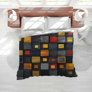 May include: A bed viewed from above, featuring a duvet cover with a geometric design. The pattern consists of squares in black, grey, gold, and red. White pillows and a sheet are visible. The bed is in a room with white walls.