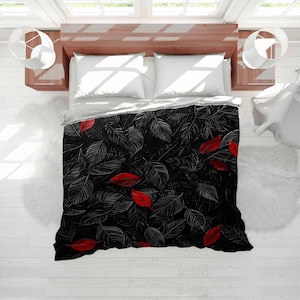 May include: A black and white leaf-patterned duvet cover with scattered red leaves. The bedding set includes white pillows and a white top sheet. The design is a modern take on a botanical theme, suitable for a bedroom.