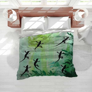 May include: A bed with a green and white comforter featuring black lizard silhouettes and green foliage. The bed is made up with white pillows and a wooden bed frame. The room has white walls and windows.
