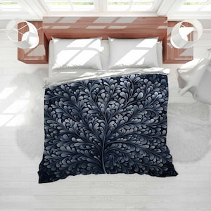 May include: A navy blue and white duvet cover featuring a stylized tree design. The tree's branches and leaves are in shades of white and grey against a dark blue backdrop. The bedding is on a wooden bed frame with white pillows.