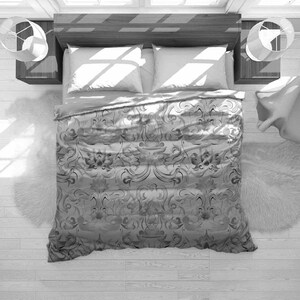 May include: An overhead shot of a bed with a patterned duvet cover and two white pillows. Two bedside tables with lamps are on either side. A fluffy rug is at the foot of the bed, with sunlight from a window.