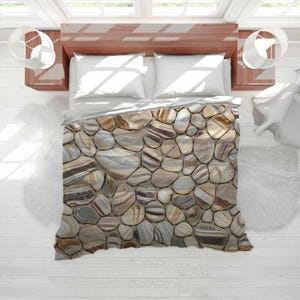 May include: A bed with a duvet cover featuring a stone pattern in shades of brown, beige, and gray. The bed has white pillows and is set against a white wooden floor. Two white lamps hang on either side of the bed.