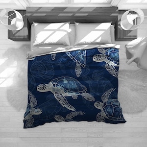 May include: A navy blue blanket featuring a pattern of sea turtles in shades of blue and white. The turtles are depicted in a detailed, artistic style, creating a marine theme. The blanket is spread over a bed with white pillows.