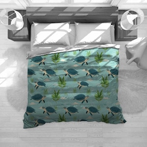 May include: A teal bedspread with a repeating pattern of blue sea turtles, green plants, and white clouds. The bedding is on a bed with white pillows and a gray top sheet. The bed is in a room with white walls and a wooden headboard.