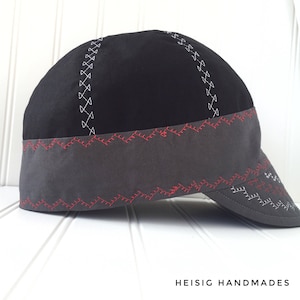 May include: A black and gray baseball cap with red and white stitching. The cap has a gray brim and a black crown with a gray band around the crown. The stitching on the cap is in a geometric pattern.
