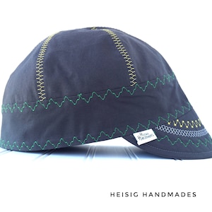 May include: A dark gray,  welding cap with green, yellow, and gray stitching. The cap has a small label that reads "Heisig Handmades".