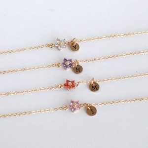 May include: Four gold chain bracelets with a small flower charm and a personalized initial charm. The flower charms are in different colors: white, purple, red, and pink.