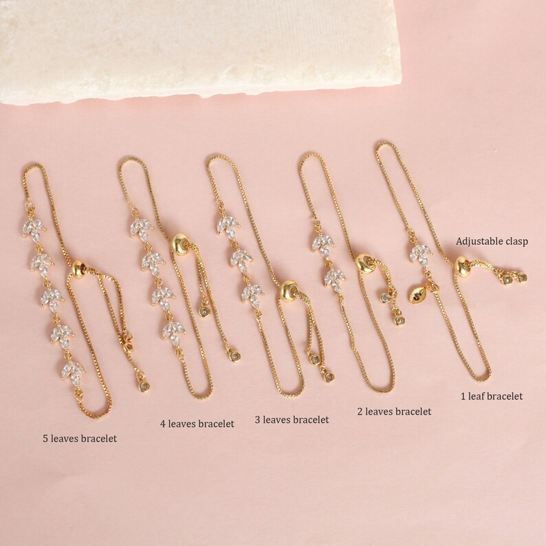 May include: Five gold chain bracelets with adjustable clasps. Each bracelet features a different number of crystal leaf charms, ranging from one to five leaves.