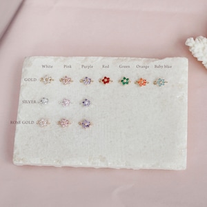 May include: A display of flower charm connectors in various colors, including white, pink, purple, red, green, orange, and baby blue. The charms are available in gold, silver, and rose gold finishes.