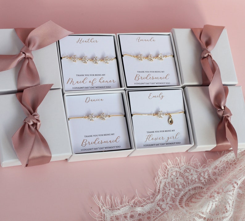 May include: Four white gift boxes with pink ribbon bows, each containing a gold bracelet with a message card. The cards read "Thank you for being my Maid of Honor", "Thank you for being my Bridesmaid", "Thank you for being my Bridesmaid", and "Thank you for being my Flower Girl".