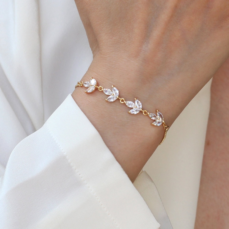 May include: A gold bracelet with a delicate chain and clear crystal leaves. The bracelet is adjustable and has a simple, elegant design.