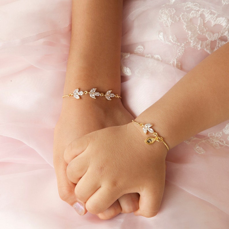 May include: Two gold bracelets with leaf-shaped charms and clear crystals. One bracelet has a small charm with the letter 'S' on it.