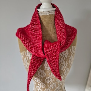 May include: A bright red knitted triangular scarf with a textured garter stitch pattern. The scarf is draped around the neck, featuring two long, pointed ends that hang down in the front, showcasing a consistent yarn weight and vibrant colour.