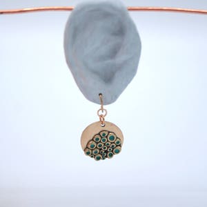 May include: A gold-toned pendant with a circular design featuring a cluster of green circles. The pendant is hanging from a thin gold chain.