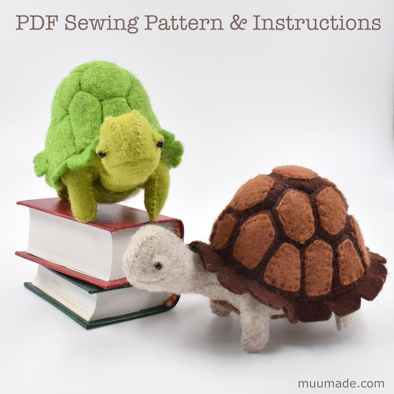 Two felt turtles, one green and the other brown. The green turtle is standing on top of a pile of two miniature books, while the brown standing in front of the green one.
