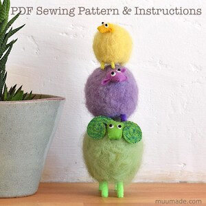 A happy fluffy sheep family: A set of 3 sewing patterns to make adorable sheep father, mother and baby! The yellow baby sheep is standing on top of its purple mother sheep, who is standing on top of the green father sheep.
