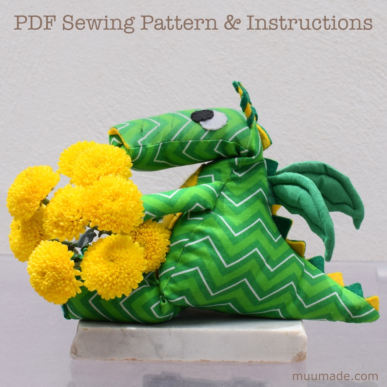 A soft green fabric dragon plushie, side view, holding a bouquet of bright yellow flowers on its lap.