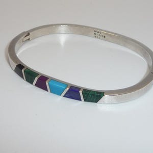 Könnte beinhalten: Silberfarbenes Armband mit eingelegten geometrischen Designs in Schwarz, Grün, Lila, Türkis und Blau. Das Armband ist mit "MAL MEXICO .925" gekennzeichnet. Ein stilvolles Schmuckstück.
