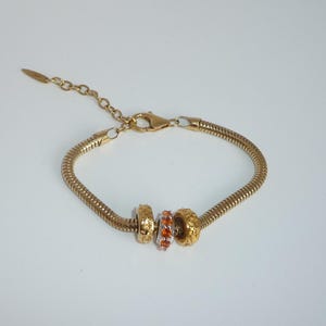May include: A gold snake chain bracelet with three gold beads. The centre bead is decorated with orange and clear crystals.