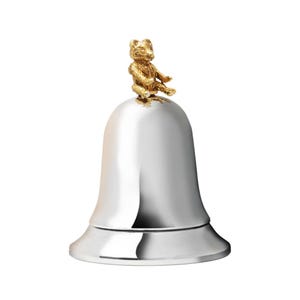 Könnte beinhalten: Eine silberne Glocke mit einer goldenen Bärenfigur auf der Oberseite. Die Glocke hat eine abgerundete Oberseite und eine breite Basis.