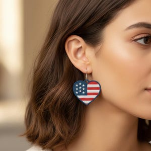 May include: Heart-shaped earrings featuring the American flag design. The earrings have a navy blue border with white stars and red and white stripes, creating a patriotic accessory.