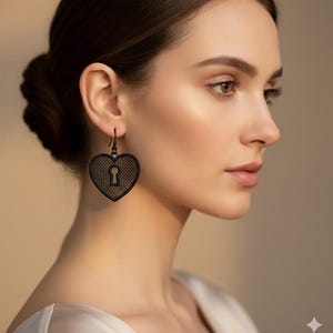 Peut inclure: Boucles d'oreilles noires en forme de cœur avec un motif de trou de serrure. Les boucles d'oreilles sont en métal foncé et présentent un motif ajouré texturé. Les boucles d'oreilles sont suspendues à un crochet. Un accessoire élégant.