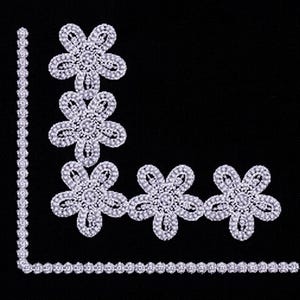 May include: White floral embellishments and a beaded trim arranged on a black background. The floral designs are symmetrical, with a central jewel surrounded by petals. The trim forms a border, creating a decorative corner.