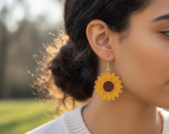 Puede incluir: Primer plano de una persona con pendientes de girasol. Los pendientes son amarillos con un centro marrón y tienen forma de girasol. Los pendientes cuelgan de ganchos plateados.
