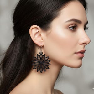 Puede incluir: Pendientes negros calados con forma de flor. Los pendientes están hechos de un material delicado y de encaje y presentan un diseño floral detallado. Los pendientes están suspendidos de ganchos plateados. Un accesorio elegante.