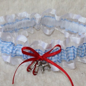 Puede incluir: Una liga de cuadros blancos y azules con ribete de encaje blanco y un lazo de satén rojo. Un dije plateado de zapatos rojos y un perro está unido al lazo. Accesorio de boda.