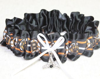 May include: Black satin garter with orange and white striped ribbon featuring a hockey puck design. A white satin bow with a rhinestone hockey stick charm hangs from the garter.