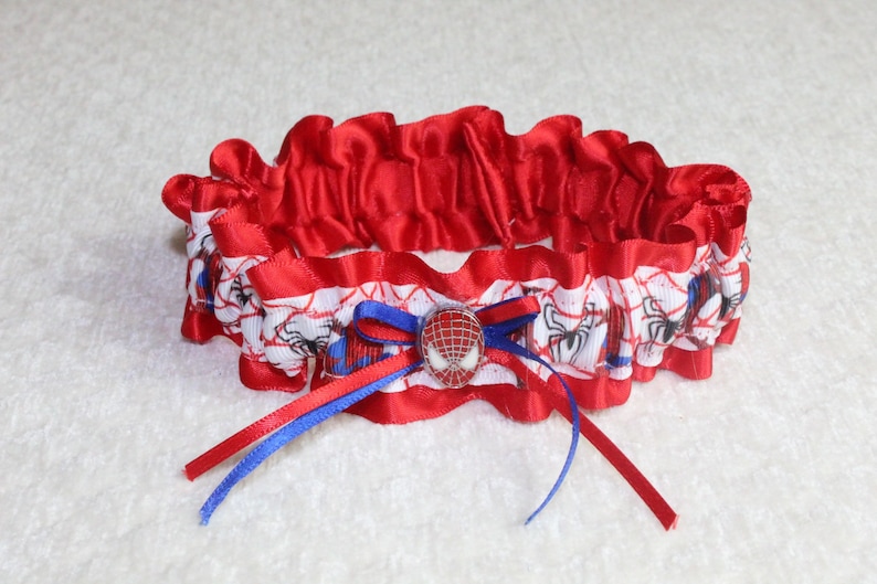 May include: Red and white satin garter with a blue and red ribbon. The garter features a Spider-Man character charm.